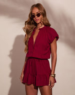 Woman wearing crimson red ruffle mini dress with drawstring waist, gold bangles, sunglasses, and wavy blonde hair