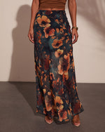 Dark floral maxi skirt with rust and amber blooms on teal background, styled with brown crop top and heeled sandals