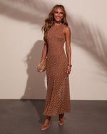 Woman in brown lace midi dress with gold accessories and clutch, smiling against neutral background