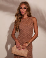 Woman in brown floral lace sleeveless dress holding beige crocodile clutch bag with gold bangle bracelets and hoop earrings
