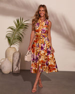 Woman wearing sleeveless floral midi dress in orange and purple print with tie waist, holding cream mini bag, styled with strappy heels