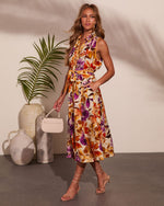 Woman in floral midi dress with orange and purple blooms, belted waist, sleeveless, styled with strappy heels and mini bag