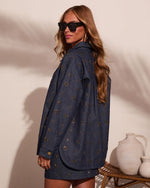 Woman wearing navy denim embellished shacket with gold starburst studs, paired with matching mini skirt and black sunglasses