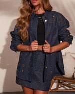 Woman wearing navy denim jacket and mini skirt set with gold starburst embellishments, layered over black crop top