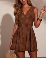 Brown polka dot mini dress with V-neckline, button front, and pleated skirt, styled with gold bangles and woven bag.