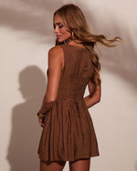 Brown polka dot sleeveless mini dress with tie waist, modeled from behind, featuring flared skirt and gold accessories