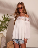 White lace crochet cold-shoulder top with flowing sleeves, styled with denim cutoff shorts and round sunglasses, boho summer look