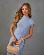 Woman in powder blue knit top and satin skirt holding woven tan leather hobo bag with gold bracelets