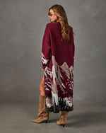 Woman in burgundy long knit cardigan with mountain landscape jacquard design, styled with tan suede knee-high boots
