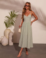 Green striped midi dress with spaghetti straps on woman wearing strappy heels, sunglasses, and cream mini bag