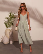 Woman wearing sage green striped midi sundress with spaghetti straps, nude lace-up heels, and cream mini bag
