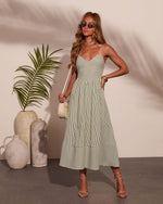 Women's green striped midi dress with spaghetti straps, fitted bodice, flowy skirt, styled with strappy heels and crossbody bag