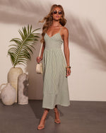Woman wearing sage green striped midi dress with spaghetti straps, nude lace-up heels, and cream crossbody bag