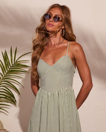 Woman in green striped spaghetti strap sundress with sweetheart neckline, gold hoop earrings, layered necklaces, and oval sunglasses
