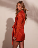 Woman wearing rust orange jacquard satin wrap mini dress with long sleeves, tie waist, and fringe detail, posed against neutral background