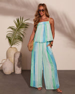 Woman wearing turquoise green striped wide-leg palazzo pants and matching spaghetti strap top with woven clutch and sunglasses