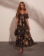 Black floral off-shoulder tiered maxi dress with golden rose print, lace-up bodice, worn with strappy heels and clutch bag