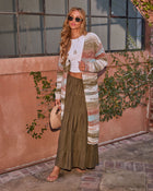 Woman wearing striped boho maxi cardigan, white crop top, olive tiered maxi skirt, tan sandals, woven bag, sunglasses