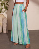 Wide-leg palazzo pants in watercolor blue and green stripes, high waist, flowy silhouette, styled with white crop top and strappy sandals