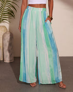 Wide-leg palazzo pants in green and blue watercolor stripe print with elastic waist, styled with white crop top and strappy sandals