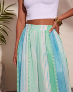 Women's striped midi skirt in aqua, mint green, and white watercolor print with elastic waist, styled with white crop top and gold bangles