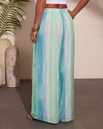Wide-leg palazzo pants in blue and green tie-dye stripe print with elastic waistband, worn with white crop top and nude heels
