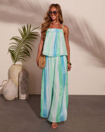 Woman wearing blue green striped maxi skirt and matching spaghetti strap top with woven bag and sunglasses