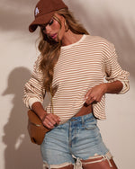 Woman wearing cream striped long-sleeve top, distressed denim shorts, brown LA cap, and tan crossbody bag in casual LA street style outfit