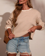 Woman wearing cream and brown striped ribbed knit top with distressed denim cutoff shorts, gold hoop earrings, and tan crossbody bag