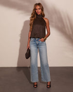 Woman wearing dark brown suede halter top, wide-leg light wash jeans, black heels, and gold bangles, holding brown clutch.