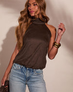 Woman wearing dark brown halter neck top with high cowl neckline, light wash jeans, gold bangles, wavy blonde hair