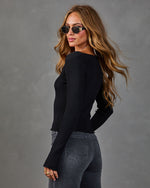 Woman wearing black ribbed long-sleeve crop top and dark gray high-waist jeans with gold sunglasses and layered necklaces