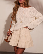 Woman wearing cream knit oversized sweater, tiered mini skirt, gold crescent necklace, and tan crossbody bag
