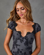 Woman wearing gray floral satin mini dress with black lace trim neckline and cap sleeves, layered gold necklaces