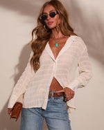 Woman wearing cream textured button-down sheer blouse, blue jeans, turquoise pendant necklace, gold hoops, and sunglasses