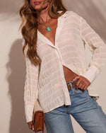 Woman wearing cream textured fringe button-down shirt, blue jeans, turquoise pendant necklace, and brown leather crossbody bag