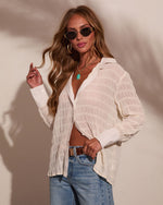Woman in sheer white textured button-down shirt, blue jeans, gold hoop earrings, turquoise pendant necklace, and retro sunglasses