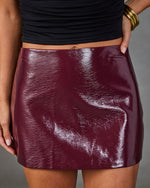 Burgundy patent leather mini skirt with glossy finish, paired with black crop top and gold bangle bracelets