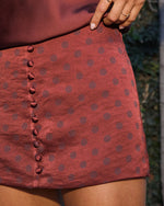Rust red polka dot satin mini skirt with decorative button detail, paired with burgundy top