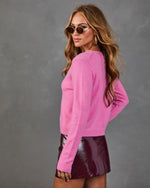 Woman wearing pink fuzzy crop sweater and burgundy patent leather mini skirt with gold hoop earrings and retro sunglasses