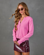Woman wearing pink knit button cardigan and burgundy patent leather mini skirt with gold hoop earrings and tinted sunglasses