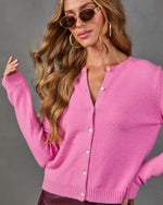 Pink knit button-front cardigan sweater on woman with wavy hair, gold hoop earrings, and brown tinted sunglasses