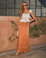 Woman in boho cream lace crop top and rust satin tiered ruffle maxi skirt with strappy heels and sunglasses