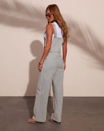 Woman wearing light wash wide-leg denim overalls with white tank top, sandals, and sunglasses, back view