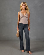 Woman wearing studded satin camisole top, dark wash wide-leg jeans, nude heeled sandals, holding woven clutch bag
