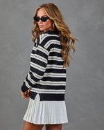 Woman wearing black and white striped oversized sweater with white pleated mini skirt and black cat-eye sunglasses