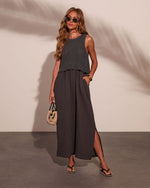 Woman wearing charcoal knit crop top layered over matching maxi dress with side slit, styled with straw bag and sandals