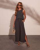 Woman wearing charcoal knit crop top layered over matching maxi dress with side slit, styled with straw bag and sandals