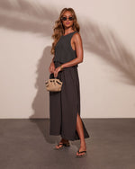 Woman wearing charcoal knit crop top over matching maxi skirt with side slit, raffia mini bag, black sandals, gold accessories