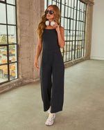 Woman wearing black wide-leg jumpsuit with white sneakers and headphones, standing in industrial loft setting